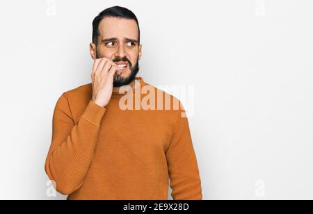 Young man with beard wearing casual winter sweater looking stressed and nervous with hands on mouth biting nails. anxiety problem. Stock Photo