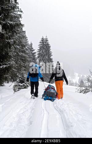 two persons back to lens pulling their baggage in winter time fogy coutryside Stock Photo