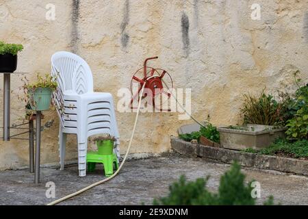 Selective focus shot of a hose reel and stacked chairs in a garden Stock Photo