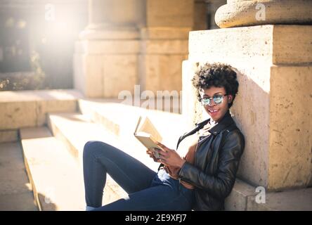 Shallow focus of an African woman with short curly hair reading a book in a park under the sunlight Stock Photo