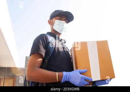 Portrait Of Young Indian Delivery Man Holding Cardboard Box Stock Photo