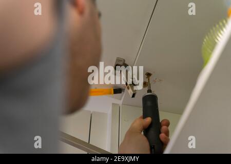 a worker fixing a kitchen cabinet with an electric screwdriver Stock Photo