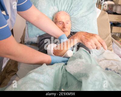 The ninety five year old has the injured arm bandaged at his house by a visiting district nurse.He is unable to leave his bed or house due to frailty Stock Photo