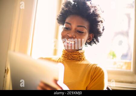 Shallow focus of a smiling African woman with short curly hair using her tablet Stock Photo