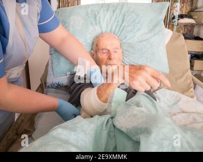 The ninety five year old has the injured arm bandaged at his house by a visiting district nurse.He is unable to leave his bed or house due to frailty Stock Photo