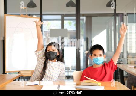 asian girl boy student wearing face mask studying raising hand in classroom. learning education at school Stock Photo