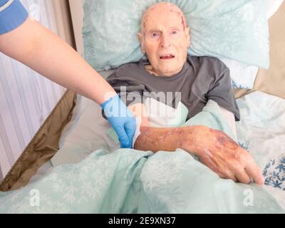 The ninety five year old has the injured arm bandaged at his house by a visiting district nurse.He is unable to leave his bed or house due to frailty Stock Photo