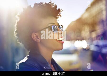 Shallow focus of a smiling African woman with sunglasses and short curly hair under the sunlight Stock Photo