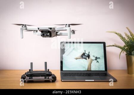 Learn how to fly drone flying in the air indoors safely with radio controller and laptop computer in the background showing online tutorial guide Stock Photo