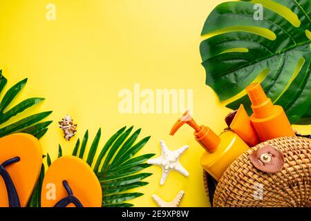 Sunscreen bottles arranged in straw bag on a bright yellow background with palm leaves, top view Stock Photo