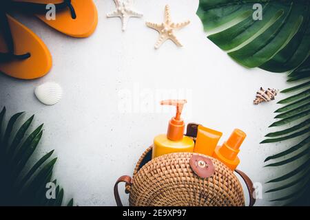 Sunscreen bottles arranged in straw bag on white background with palm leaves, top view Stock Photo
