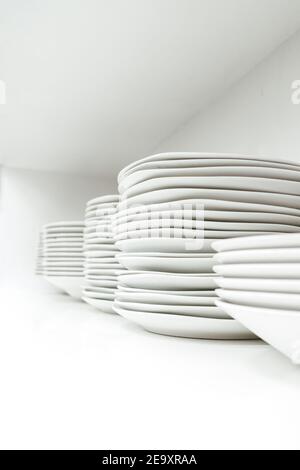 Pile of simple similar ceramic plates placed on each other against white background in kitchen cupboard Stock Photo