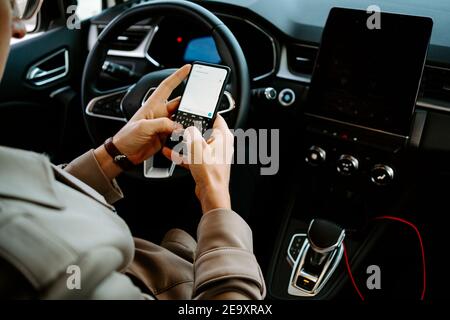 Crop unrecognizable male entrepreneur sitting on driver seat in luxury automobile and browsing mobile phone Stock Photo