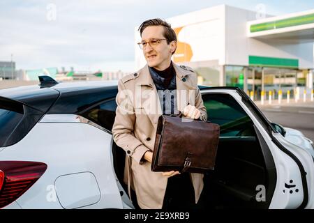Confident male entrepreneur in coat and with attache case getting out of modern automobile and looking away Stock Photo
