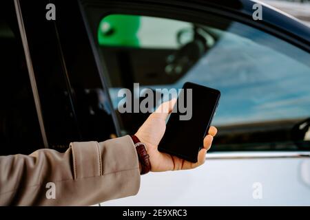 Male entrepreneur unlocking door of modern automobile with smartphone while using remote control app Stock Photo