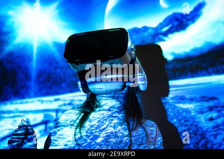 Unrecognizable young girl in casual wear and VR headset getting new experience and touching virtual object in room with colorful projector illuminatio Stock Photo