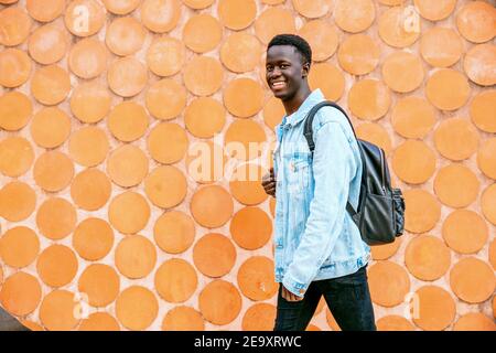 Young black man with denim jacket and backpack looking at the camera while walking Stock Photo