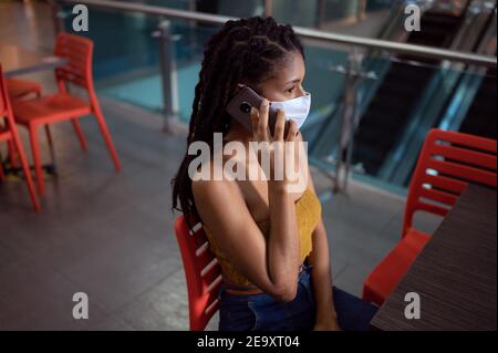 Portrait of attractive young afro latin Woman wearing a facemask and talking on smartphone in a commercial mall, Colombia Stock Photo