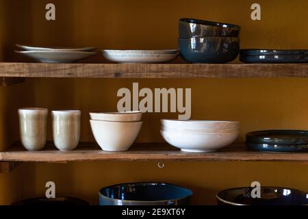 Set of various dishware consisting of plates cups and bowls placed on wooden shelves Stock Photo