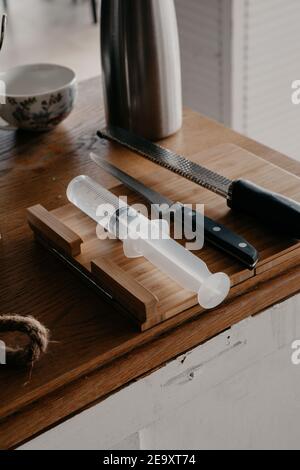 From above of various sharp knives and culinary syringe placed on wooden cutting board in kitchen Stock Photo