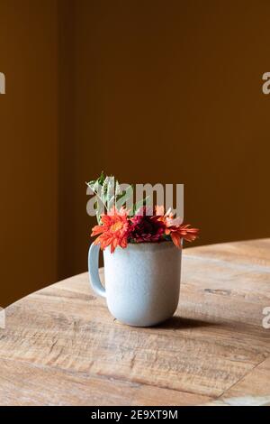 Ceramic cup with fresh blooming flowers placed on wooden table in restaurant in daylight Stock Photo