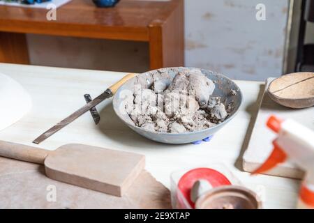 From above bowl with soft clay placed on wooden table near set of potter tools in workshop Stock Photo