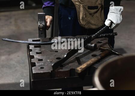 High angle of crop anonymous craftsman hitting metal detail with hammer while working in forge Stock Photo