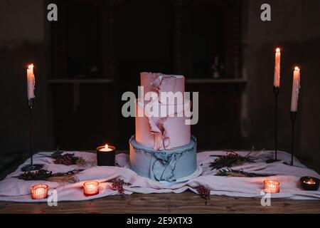 Delicious tiered cake served on wooden table and surrounded by burning candles in dark room Stock Photo