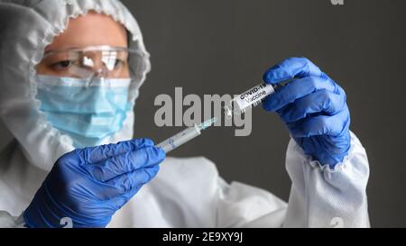Coronavirus vaccine in doctor hands, nurse in medical PPE suit holds syringe and bottle with vaccine for COVID-19 cure. Concept of corona virus treatm Stock Photo