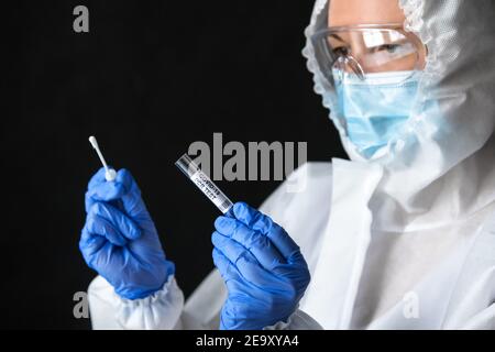 Coronavirus swab collection kit in doctor hands, nurse in medical personal protective equipment (PPE) holds COVID-19 PCR test on dark background. Conc Stock Photo