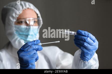 COVID-19 swab collection kit in doctor hands, nurse in personal protective equipment (PPE) suit holds tube of coronavirus PCR test. Concept of corona Stock Photo