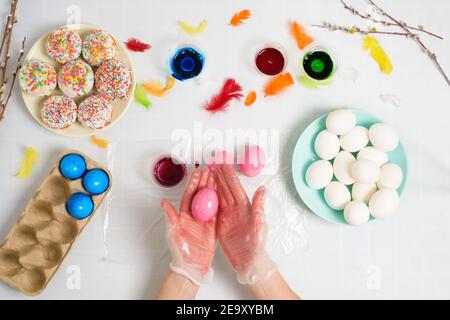 the process of coloring eggs for Easter in blue and red colors. a woman in gloves paints eggs with dye from a jar, top view, willow branches and color Stock Photo