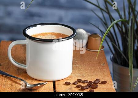 A white coffee cup with cream coffee stands on a colored wooden wooden surface. Coffee beans are next to it Stock Photo