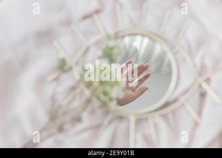 Hand reflected in mirror on background of soft fabric with manuka flowers. Spring aesthetics. Mental Health concept. Gentle image. Eye shape boho mirr Stock Photo