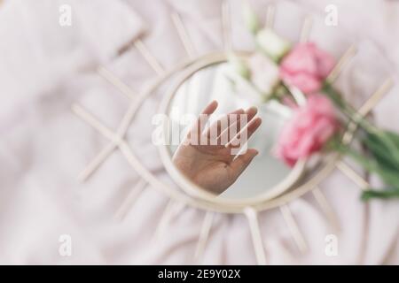 Hand reflected in mirror on background of soft fabric with eustoma flowers. Spring aesthetics. Mental Health concept. Gentle image. Eye shape boho mir Stock Photo