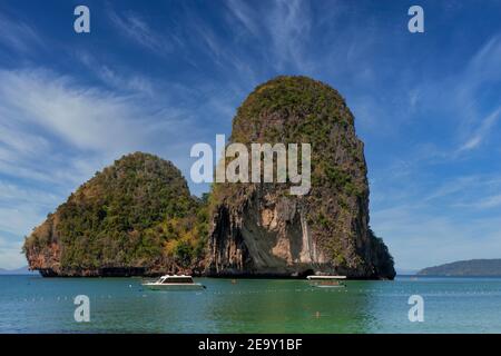 A giant rock formation overshadows the blue sea at Railay Beach in Krabi, Thailand Stock Photo