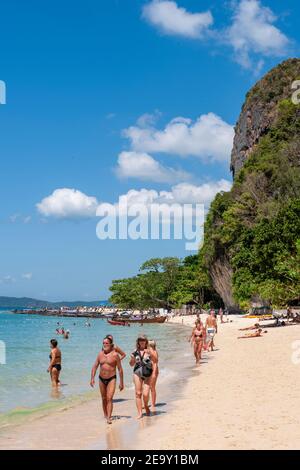 A giant rock formation overshadows the white sand and blue sea of Railay Beach, in Krabi, Thailand Stock Photo