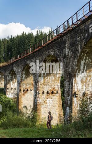 Woman standing under ancient railway viaduct in Carpathian village Vorokhta, Ukraine. Stock Photo