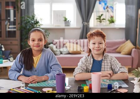 Portrait of two children sitting at the table and looking at camera while learning to paint together at home Stock Photo