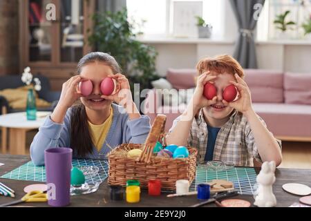 Portrait of two children sitting at the table and painting Easter eggs at home Stock Photo