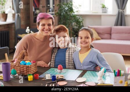 Portrait of happy family smiling at camera while sitting at the table and painting eggs for holiday together at home Stock Photo