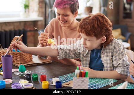 Mother sitting at the table and painting eggs together with her son they preparing for Easter together Stock Photo