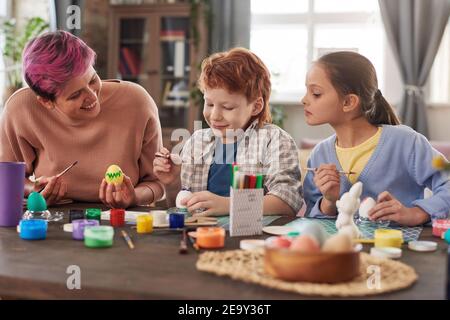 Happy family of three painting and decorating eggs at the table preparing for Easter at home Stock Photo