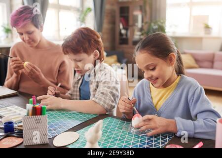 Mother painting eggs for Easter together with her children at the table at home Stock Photo