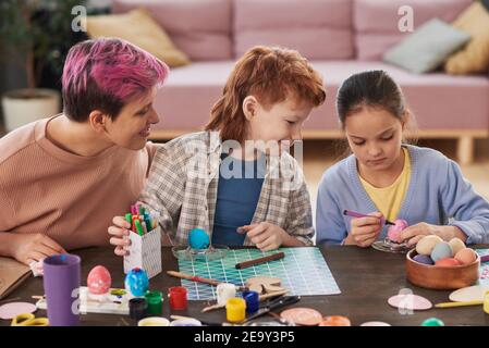 Mother with her children sitting at the table and painting eggs with crayons they preparing for Easter Stock Photo