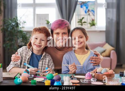 Portrait of happy mother with her two children smiling at camera while decorating and painting eggs for Easter Stock Photo