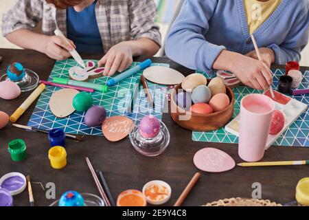 Close-up of people sitting at the table painting eggs with paintbrushes they preparing for Easter together Stock Photo