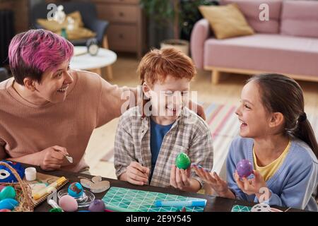 Mother with her children sitting at the table with Easter eggs and having fun together at home Stock Photo