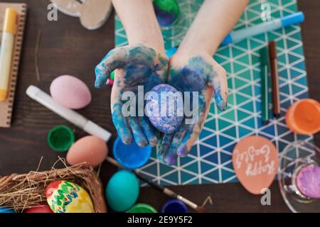 High angle view of child holding painted egg in his hands he painting eggs for Easter at the table Stock Photo