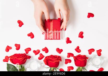 Female hands hold gift box for valentine's day. Red roses and candles on a white background. Stock Photo